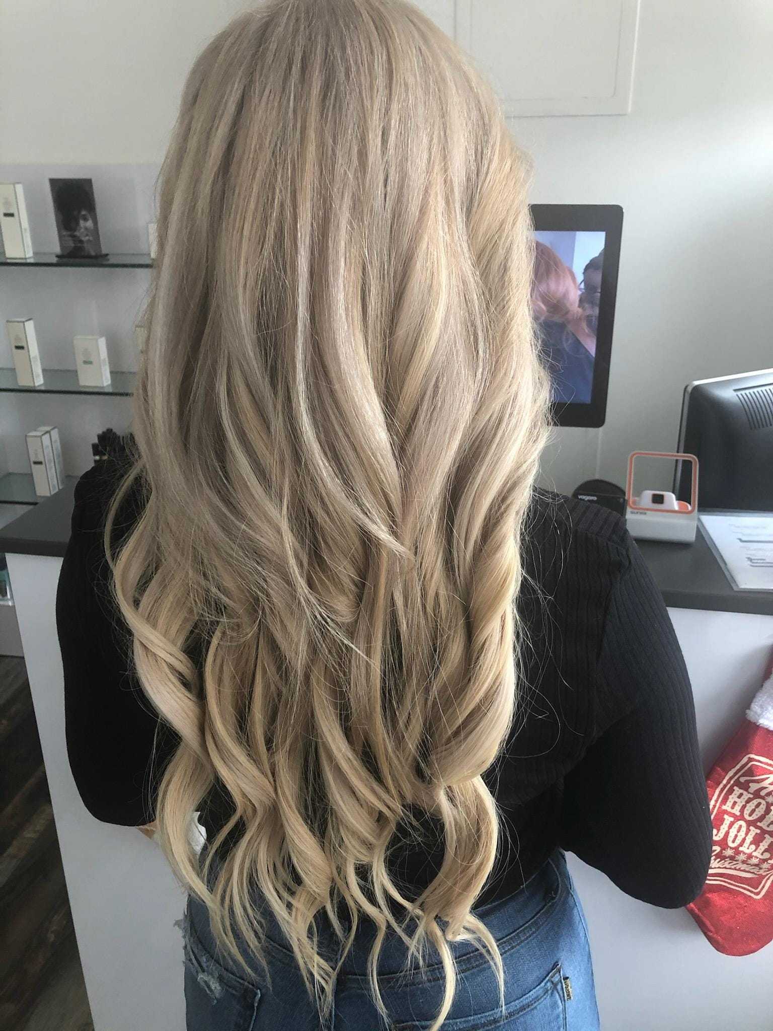 Long wavy blonde hair viewed from the back in a salon setting.